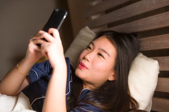 ベッドでスマートフォンを操作する女性